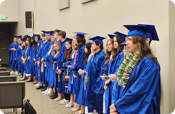 High school students lined up wearing blue cap and gown during graduation.