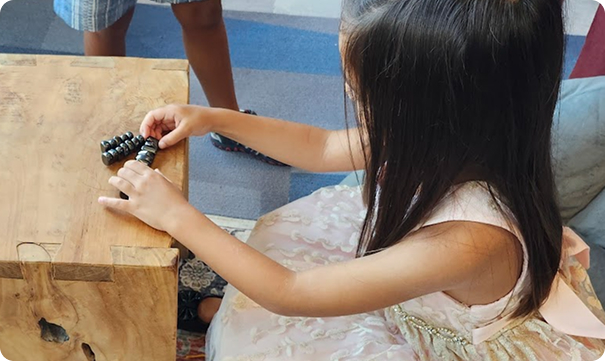 Young student playing with small objects on a wooden table during a hands-on learning activity.