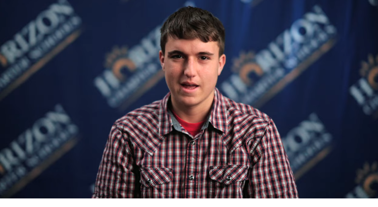 Student James wearing plaid shirt with horizon logo in background